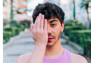 man with makeup covering his face with his hand in protest against homophobia